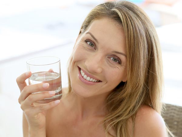 Frau mit Wasserglas in der Hand lächelt in die Kamera