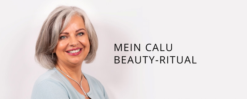 „Porträt der lächelnden Frau CLaudia Fischer mit schulterlangem grauem Haar und hellem Oberteil vor neutralem Hintergrund. Rechts daneben steht der Text ‚Mein Calu Beauty-Ritual‘.“