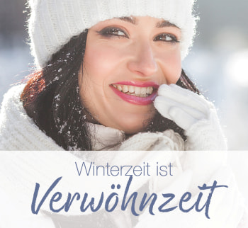 Lächelnde Frau in Winterkleidung mit Mütze und Handschuhen, hält sich die Hand an den Mund; Text: „Winterzeit ist Verwöhnzeit“.